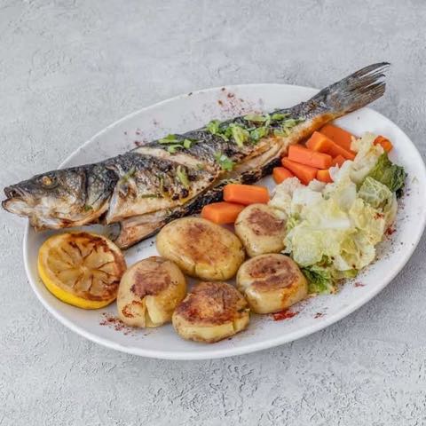 A whole grilled fish with potatoes, carrots and cabbage