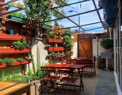 Outdoor tables under a pergola, with red painted furniture and plants